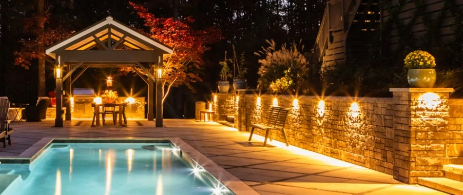 Outdoor lights on a retaining wall and outdoor kitchen beside a pool in Cary, NC.