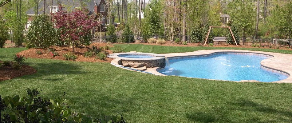 Grass and landscaping around a backyard pool in Neuse, NC.